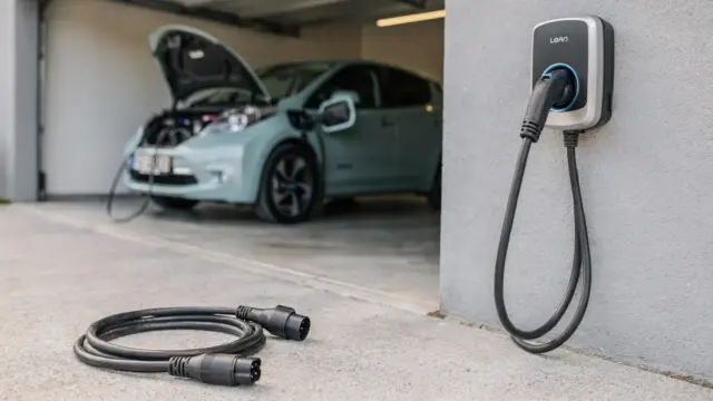 Typ-1-auf-Typ-2-Adapter an einer Wallbox neben einem älteren Elektroauto mit Ladeanschluss