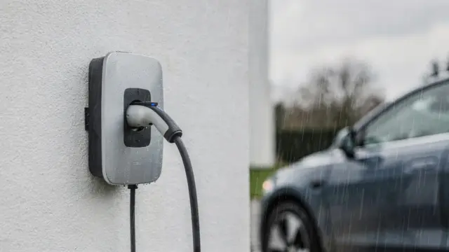 Wallbox bei Regen an der Hauswand mit angeschlossenem E-Auto im Außenbereich