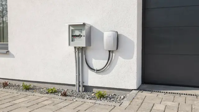 Wallbox am Hausanschluss vor einem Einfamilienhaus mit Technikschrank und Ladepunkt