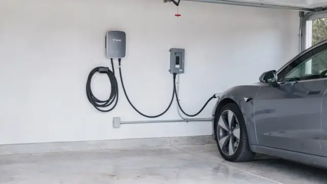 11-kW-Wallbox in der Garage an der Wand neben Elektroauto und Sicherungskasten