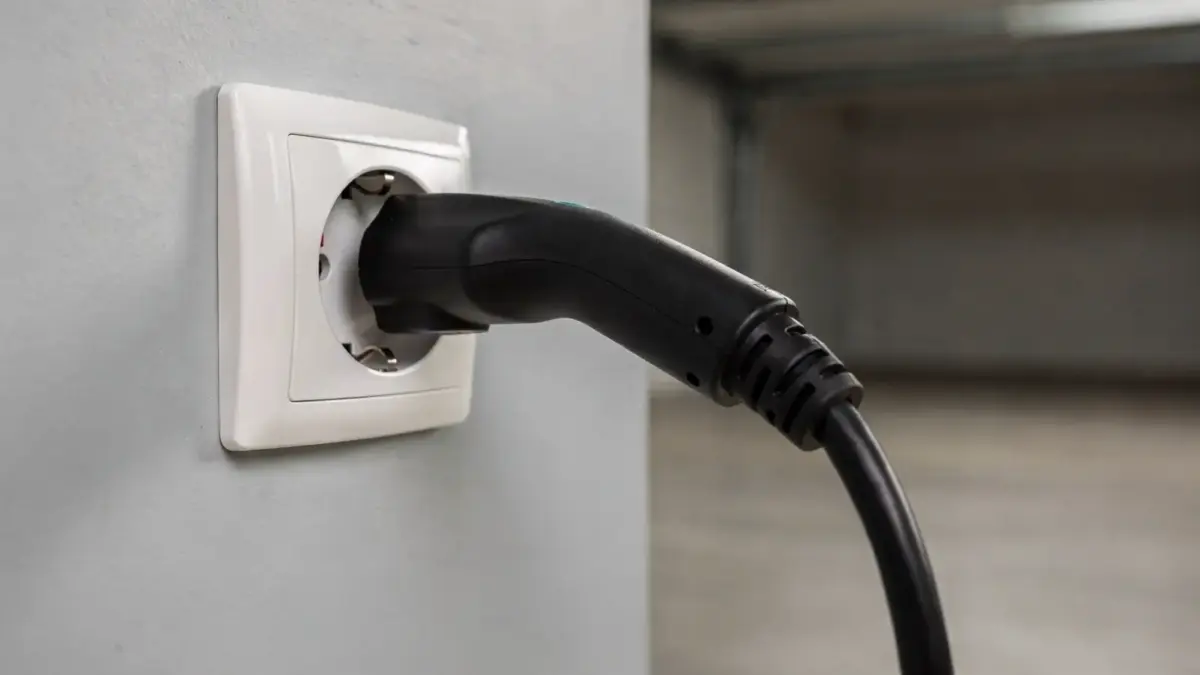 Nahaufnahme einer Schuko-Steckdose mit eingestecktem Ladekabel in einer Garage beim Laden eines E-Autos